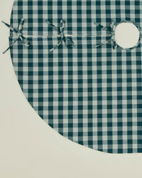 The Hawkins New York Essential Gingham Tree Skirt in Sky/Peacock is a circular cotton skirt with a green and white gingham pattern, four fabric ties along the opening, and a center hole. It is displayed flat on a light surface.