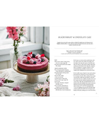 A pink and brown, plant-based layered cake topped with berries and flowers is displayed on a glass stand with pink blooms. On the right is the recipe text for blackcurrant and chocolate cake from Cozy Publishing's Vegalicious Cheesecakes.