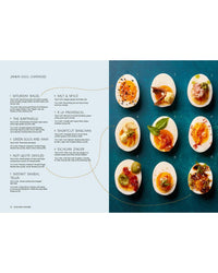 Snacking Dinners by Chronicle Books features nine halved jammy eggs with creative toppings on a blue background—ideal for self-care meals. An ingredient menu at left suggests names and ideas for unique egg garnishes.
