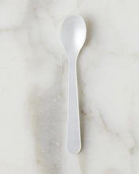 The etúHOME Acrylic Dipping Spoon in Pearl rests on a white marble surface with light gray and beige veining, bringing a playful touch as a chic entertaining accessory.
