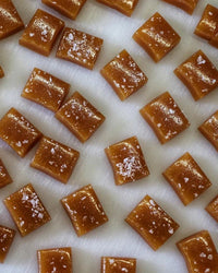 Close-up of Wildflower Caramel Co's Salted Caramels in A Bag, neatly arranged and sprinkled with flaky sea salt on a white surface.