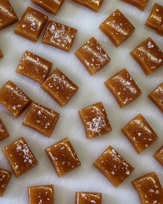 Close-up of Wildflower Caramel Co's Salted Caramels in A Bag, neatly arranged and sprinkled with flaky sea salt on a white surface.