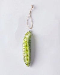 The Cody Foster Garden Pea - Light Green Ornament features a hand-crafted green pea pod shape with glitter accents and a twine loop for hanging, shown against a plain white background.