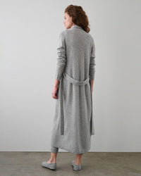 A woman stands facing away in a minimalist room, wearing the White + Warren Cashmere Long Robe in Grey Heather, styled with matching gray pants and slippers.