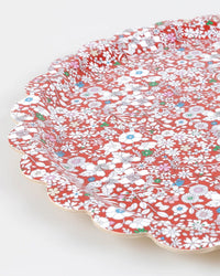 A close-up of the Meri Meri x Liberty Red June's Meadow Small Tray, featuring a scalloped edge and dense floral patterns in white, blue, green, and red on a vibrant red background.
