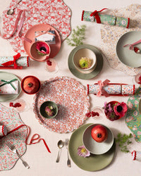 A festive table is set with floral plates, pink and green dishes, pomegranates, flowers, crackers, cutlery, ribbon, handwritten place cards, and the Meri Meri x Liberty Red June's Meadow Small Tray on a light tablecloth.