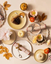 A festive autumn table features floral plates, ribbon-tied crackers, small pumpkins, decorative leaves, spoons, pastel flowers, and a charming Meri Meri x Liberty June's Meadow Small Tray on a beige background.