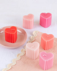 Five Meri Meri X Liberty Scalloped Heart Candles in pink and red, arranged on a scalloped white cloth, with one on a pink dish—a charming Valentine’s gift from Meri Meri.
