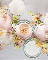 Meri Meri Cream Decagon Compostable Dinner Plates are artfully arranged on a white surface and adorned with soft pink, cream, and yellow flowers for a delicate, elegant display.