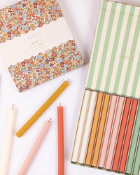 The Meri Meri x Liberty June Blossom Candle Gift Box, featuring colorful ridged candles, is displayed with its floral-patterned lid, with several striped candles arranged beside the Liberty-inspired box.