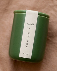 A 4 oz green ceramic jar candle from LEIF, labeled Neroli & Cotton, rests on a beige fabric background.