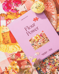 The Flour Power - Better Homes & Gardens Collab 1000 Piece Puzzle by Piecework Puzzles adds home-baked charm with its pastel purple box, dessert-themed design, yellow pieces, and cupcake details—ideal for vintage cookbook fans.