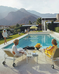 Women lounge by a pool at a mid-century house with mountains behind, echoing the iconic scene from Slim Aarons’ Poolside Gossip. Experience it with the Piecework Puzzles Poolside Gossip - Slim Aarons Collab 1000 Piece Puzzle.