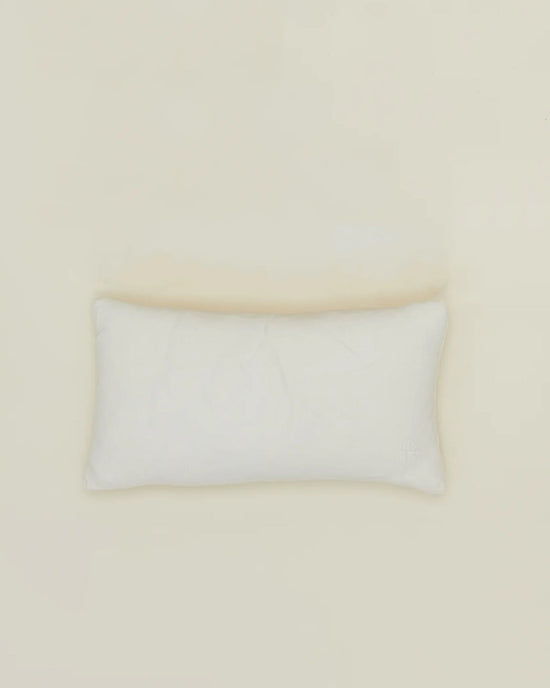 The Hawkins New York Simple Linen Pillow (22 x 12 inches, Ivory) with a plush down insert rests on a light beige surface, shot from above with minimal shadows. The machine-washable cover allows for easy care.