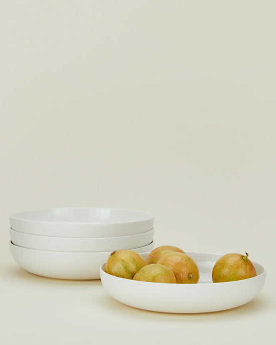 Three Simple Porcelain Low Bowls - Set of 4 by Hawkins New York are shown, with one bowl filled with passion fruits, all against a plain background. Bring the elegance of Hawkins New York porcelain dinnerware into your home.