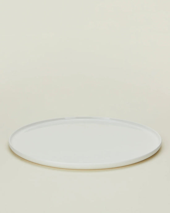 A Simple Porcelain Salad Plate from Hawkins New Yorks set of 4 is displayed empty on a light beige background, viewed from a slight angle. The plain, round white plate evokes fine dinnerware style.