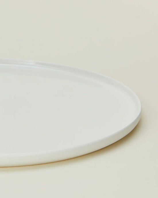 A close-up of the Hawkins New York Simple Porcelain Salad Plates (Set of 4) shows a portion of one sleek, round plate against a light beige background.