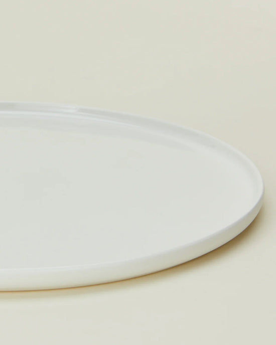 A close-up of a Hawkins New York Simple Porcelain Dinner Plate from the Set of 4, partially visible on a light beige surface.