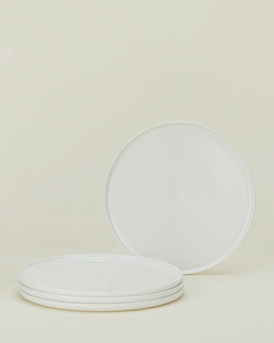 A set of four Simple Porcelain Salad Plates by Hawkins New York is stacked, with one plate upright behind the stack, shown against a neutral light background.