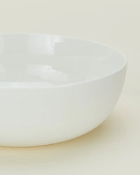 A close-up of the Simple Porcelain Serving Bowl by Hawkins New York, featuring a round shape, smooth edges, and a glossy white porcelain finish on a light, neutral background.