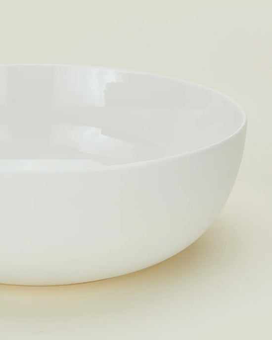 A close-up of the Simple Porcelain Serving Bowl by Hawkins New York, featuring a round shape, smooth edges, and a glossy white porcelain finish on a light, neutral background.