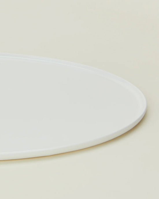 Close-up of the Hawkins New York Simple Porcelain Serving Platter—partially visible—showcasing its clean, white design against a light beige background.