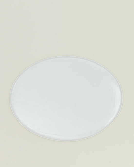 The Simple Porcelain Serving Platter by Hawkins New York, an oval white dish with a glossy finish, sits centered on a light beige background, showcasing the refined elegance of porcelain dinnerware.