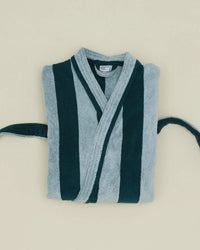 A folded Hawkins New York Simple Striped Terry Bathrobe in Sky/Peacock, featuring wide vertical stripes, a belt, and a shawl collar, is displayed on a pale beige background.