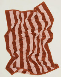 A crumpled Hawkins New York Simple Striped Terry Bath Sheet in Blush/Terracotta, featuring wide alternating stripes, rests on a light surface.