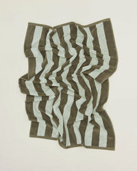 A Simple Striped Terry Bath Towel in Olive/Sage by Hawkins New York, featuring wide horizontal stripes, lies crumpled on a flat, light-colored surface.