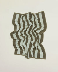A Hawkins New York Simple Striped Terry Hand Towel in Olive/Sage, featuring wide alternating dark and light stripes, lies flat on a light surface with a slightly wrinkled appearance.