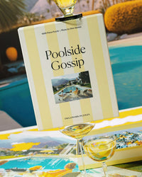 The Poolside Gossip - Slim Aarons Collab 1000 Piece Puzzle by Piecework Puzzles is balanced on two wine glasses by the pool, with its completed midcentury-inspired design and a sunny outdoor scene in the background.