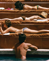 Relax poolside with Piecework Puzzles’ Sun Basking—Slim Aarons Collab 1000 Piece Puzzle, featuring four sunbathers on terraced steps in swimsuits and straw hats, echoing classic Slim Aarons photography.