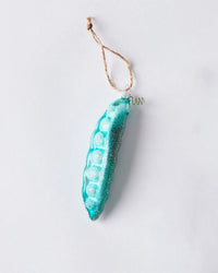 The Cody Foster Garden Pea - Teal Green Ornament features a turquoise glass pea pod with glitter accents and a brown twine loop for hanging, shown against a plain white background.