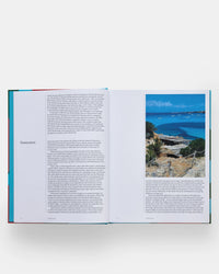 An open copy of The Spanish Mediterranean Islands Cookbook by Phaidon Press displays text about Formentera alongside a vibrant photo of its rocky coastline and blue sea, with additional details below on Balearic Islands cuisine.