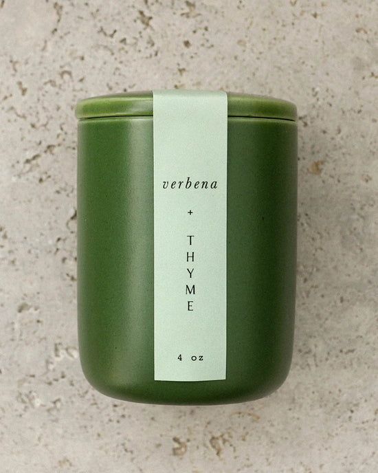 A green ceramic jar labeled Verbena & Thyme 4 oz by LEIF features a soy wax blend and wooden wick, set on a speckled stone surface.